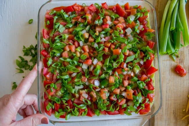 onions and tomatoes layered on top of bean dip.