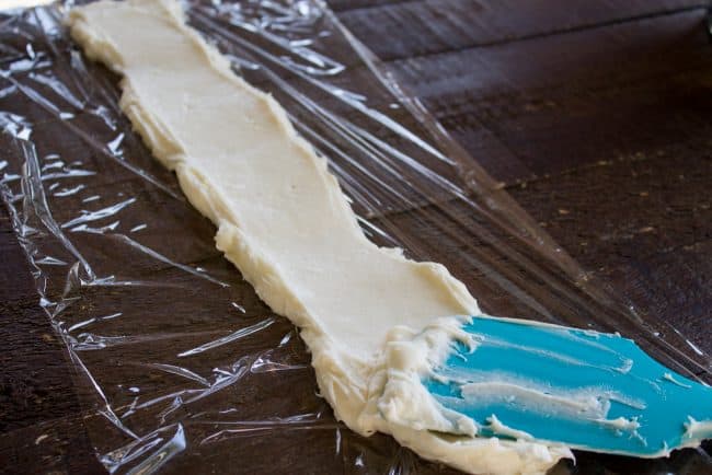 spreading cream cheese on plastic wrap with spatula.
