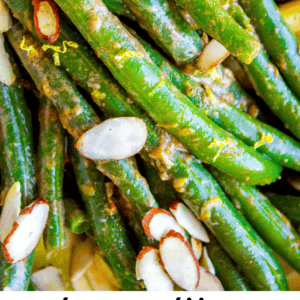 Close-up of green beans topped with sliced almonds and lemon zest, all coated in a zesty lemon Dijon sauce. Text at the bottom reads: lemon dijon green beans almondine - The Food Charlatan.