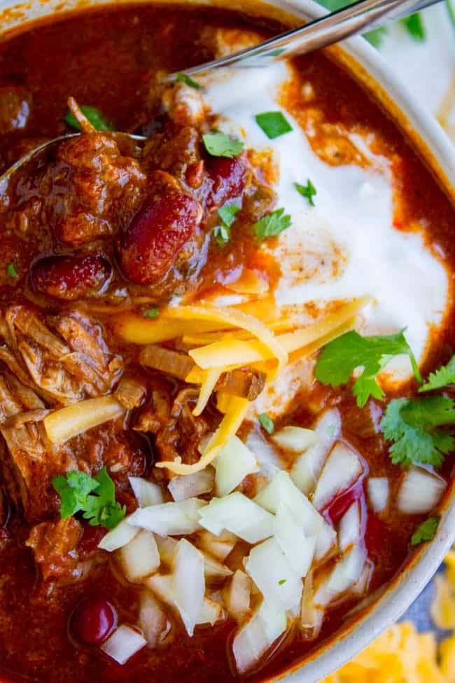 bowl of chili shot from overhead topped with cheddar, sour cream, onions, and cilantro. 