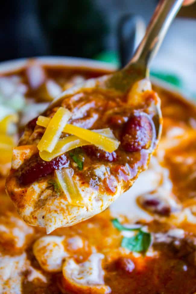 a spoonful of chili topped with cheddar, sour cream, and cilantro being lifted from a bowl.