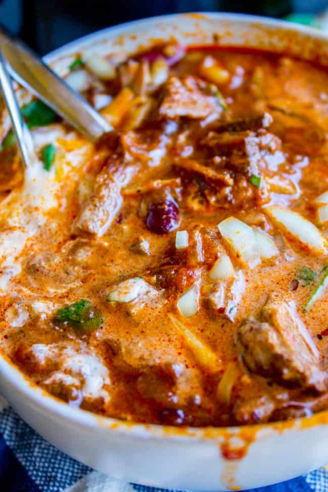 chili in a bowl with two metal spoons topped with onions, cilantro, and sour cream. 