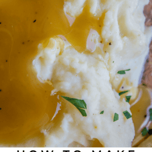 Close-up of creamy mashed potatoes topped with rich brown gravy and garnished with fresh herbs. Text at the bottom reads: “Creamy Mashed Potatoes - The Food Charlatan.”.