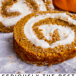A close-up of a pumpkin roll cake with creamy white filling, sliced to reveal the spiral pattern. Pumpkins decorate the background. Text at the bottom reads, “Seriously the ultimate pumpkin roll of your life.”.