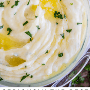 A bowl of creamy mashed potatoes topped with melted butter and sprinkled with chopped parsley, viewed from above. Text below reads: Seriously Creamy Mashed Potatoes. The Food Charlatan.