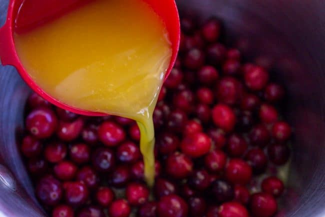 pouring orange juice into a pot with fresh cranberries.