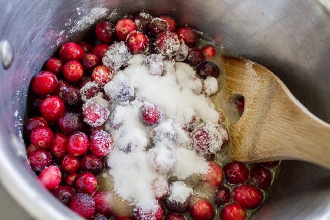 stirring sugar into cranberries in a pot.