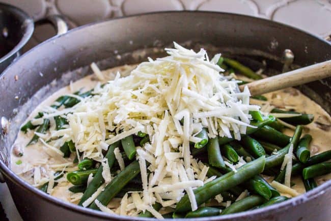 adding parmesan cheese and blanched green beans to creamy mushroom sauce in a pan.