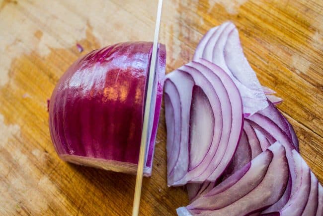 slicing red onions on a wooden cutting board. 