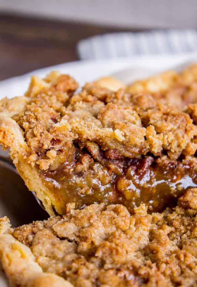 a slice of gooey toffee pecan pie with streusel being lifted from the whole pie. 