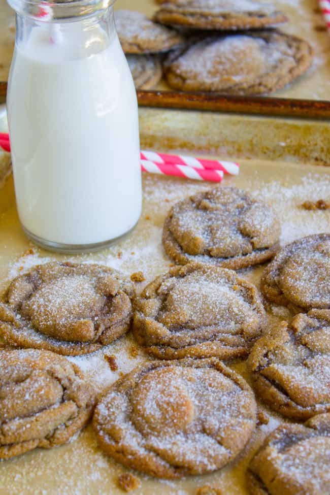 molasses cookies cooling on cookie sheets with a tall bottle of milk and red and white striped straws.