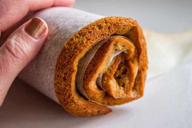 rolling pumpkin cake into a log with parchment paper.