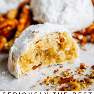 Close-up of powdered sugar-coated Mexican wedding cookies, one with a bite taken out, revealing a crumbly inside with chopped pecans. Text below reads Seriously delicious Mexican Wedding Cookies.