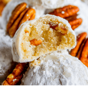 A close-up of powdered sugar-coated Mexican wedding cookies with pecans. One cookie is split to reveal its crumbly, nutty inside. Text overlay reads: “Classic Mexican Wedding Cookies – The Food Charlatan.”.