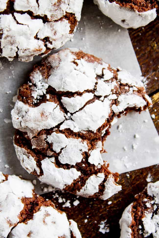 chocolate crinkle cookies on a sheet of parchment paper, one with a bite taken out of it.