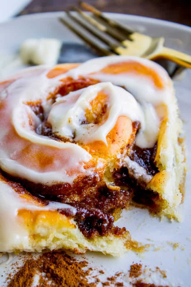 fluffy iced cinnamon roll on a plate with a fork in the background.