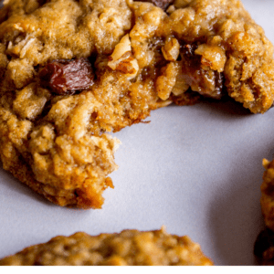 A close-up of a soft and chewy oatmeal raisin cookie with a bite taken out, surrounded by more cookies. Text below reads: Soft & Chewy Oatmeal Raisin Cookies - The Food Charlatan. Perfect for dessert lovers.