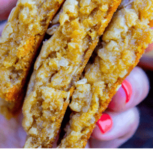 A close-up of two hands holding thick, chewy peanut butter oatmeal cookies with visible oats. Text below reads: Melt in your mouth peanut butter oatmeal cookies. The Food Charlatan’s favorite treat.