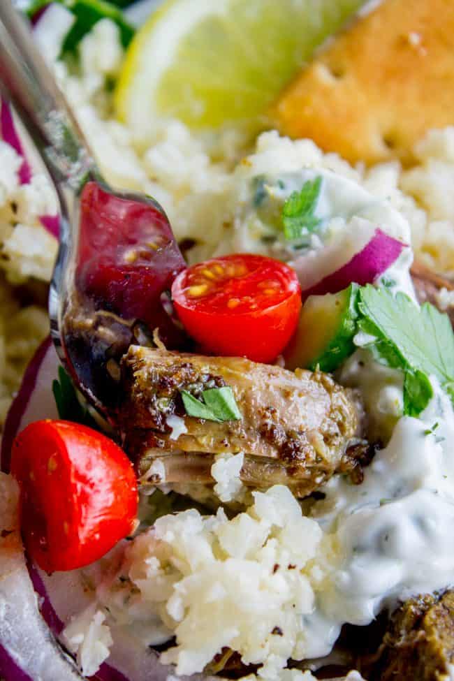 lifting a forkful of shredded beef with cauliflower rice, tzatziki sauce, fresh veggies, and herbs.
