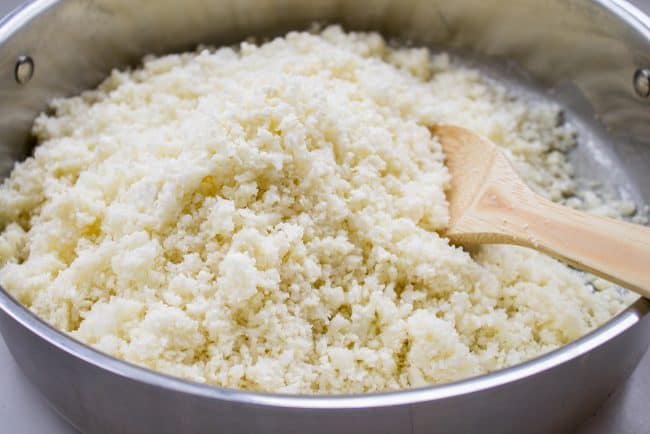 cooking cauliflower rice in a pan with a wooden spoon. 