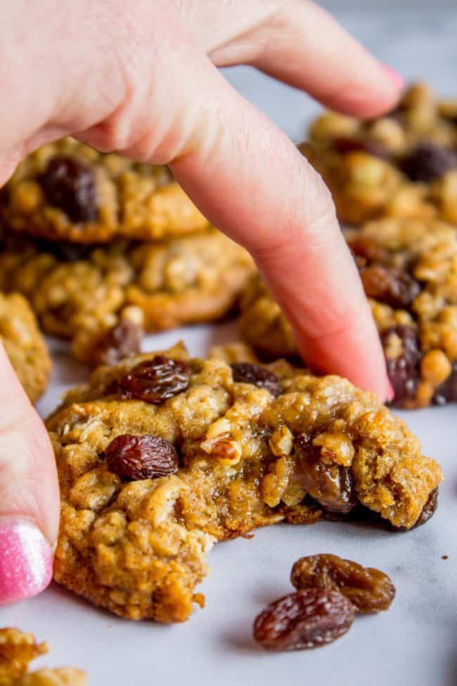 hand lifting an oatmeal raisin cookie with a bite taken out of it.