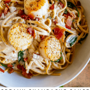 A white bowl filled with pasta topped with creamy sauce, pan-seared scallops, crispy bacon bits, and spinach, garnished on a rustic surface with a striped towel. Text overlay reads: “Pan-Seared Scallops pasta.”.