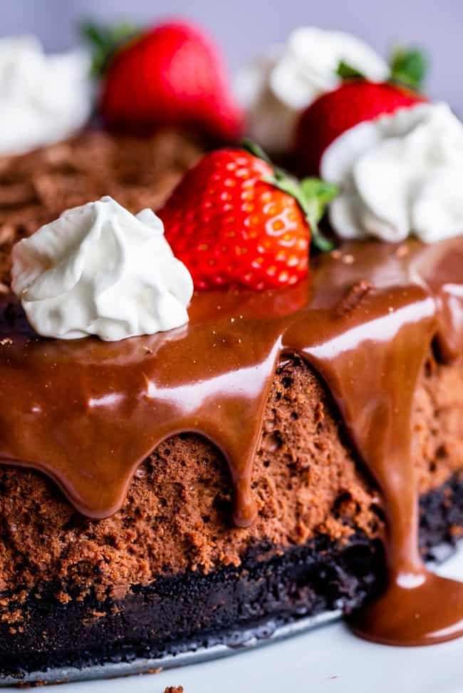 a decadent chocolate cheesecake with an Oreo crust, chocolate ganache, strawberries, and whipped cream shot up close.