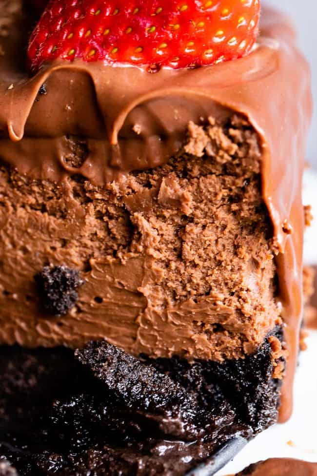 a closeup shot of rich chocolate cheesecake with chocolate ganache and a strawberry on top.