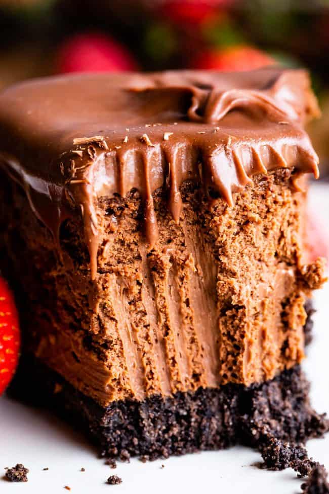 a slice of chocolate ganache topped chocolate cheesecake with forkfuls removed.