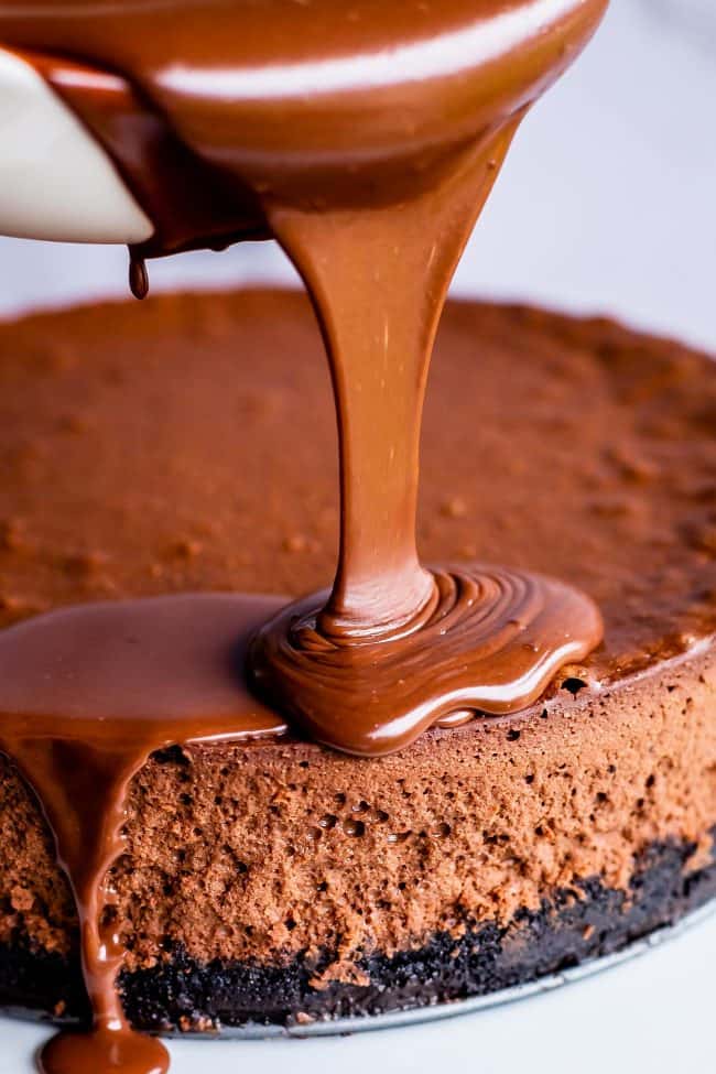 pouring chocolate ganache on a chocolate cheesecake with an Oreo crust.