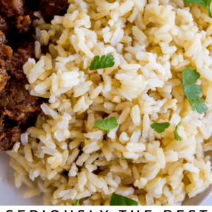 Close-up of a plate with fluffy Instant Pot brown rice garnished with parsley, next to a serving of meat. Text reads: “Seriously the best Instant Pot brown rice. The Food Charlatan.”.