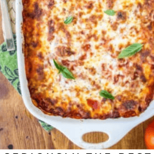 A baked ravioli lasagna in a white casserole dish, topped with melted cheese and fresh basil leaves, with a serving spoon resting inside. Text below reads: Seriously Good Ravioli Lasagna - The Food Charlatan.