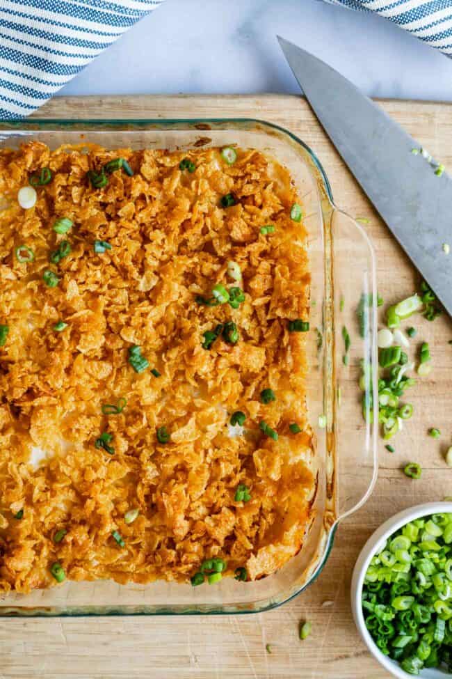 funeral potatoes in a clear glass dish shot from overhead, with green onions and chef's knife.