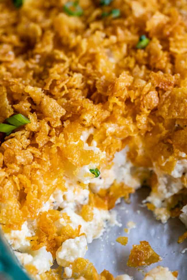 cheesy potatoes topped with cornflakes in a pan with a serving missing.