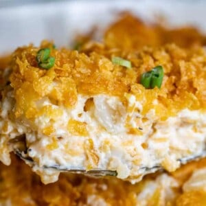 A close-up of funeral potatoes, a cheesy potato casserole with a crispy golden topping, garnished with chopped green onions.