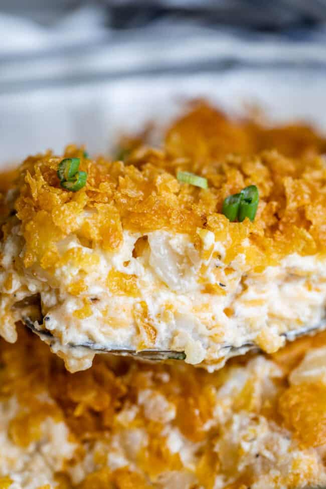 spoon lifting cheesy potato casserole from dish, topped with green onions.
