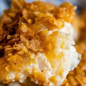 Close-up of creamy funeral potatoes, topped with a golden, crispy layer of cornflakes, showing a crunchy texture and melted cheese.