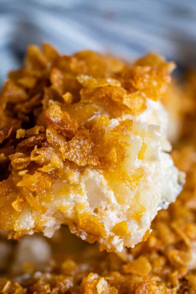 funeral potatoes topped with cornflakes being lifted from a casserole dish. 