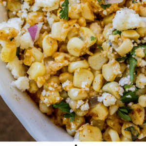 A close-up of Mexican street corn dip with corn, crumbled cheese, chopped red onion, cilantro, and tortilla chips in a white dish. The text below reads “Mexican Street Corn Dip – The Food Charlatan,” highlighting its vibrant flavors.