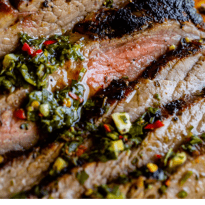 sliced flank steak on a wooden cutting board with chimichurri sauce.