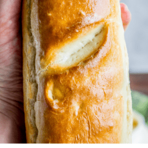 A hand holds a shiny, golden-brown loaf of French bread. Text below reads: “The Food Charlatan: fresh French bread in one hour.”.