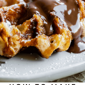 Close-up of golden Liege waffles drizzled with chocolate sauce and sprinkled with powdered sugar on a plate. Text below reads: Liege Waffles Guide - The Food Charlatan.