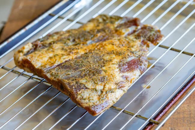 a marinated flank steak on a cooling rack over a baking sheet, ready to be broiled in the oven. 