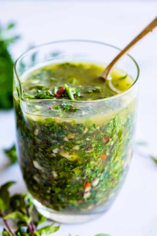 chimichurri sauce in a tall glass cup with a spoon.