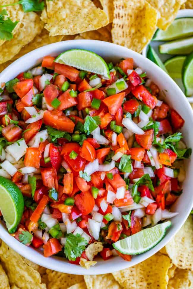 pico de gallo in a white bowl with lime wedges and tortilla chips.