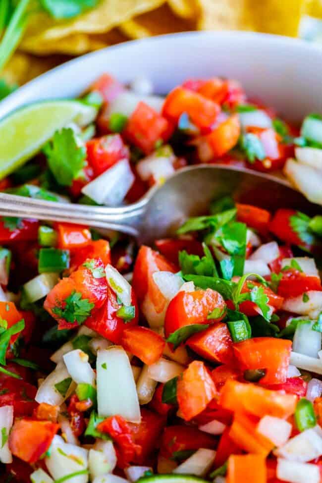 pico de gallo in a white bowl with a metal spoon.