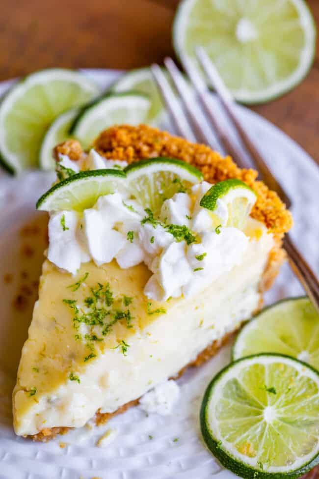 a slice of key lime pie with whipped cream and lime slices on a plate with a fork.
