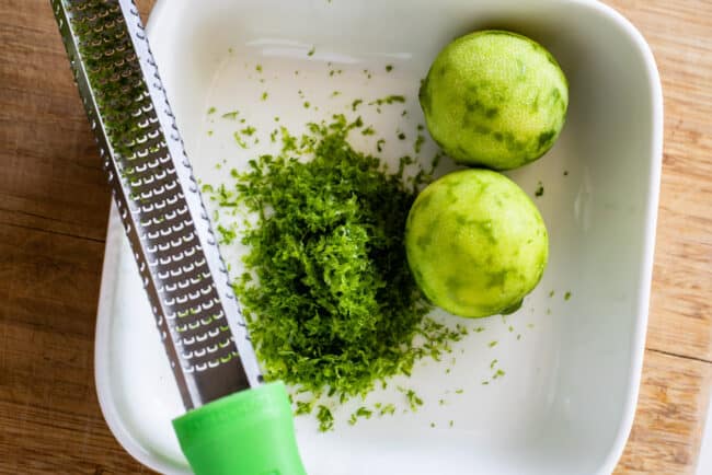 two limes zested in a white dish with a microplane grater.