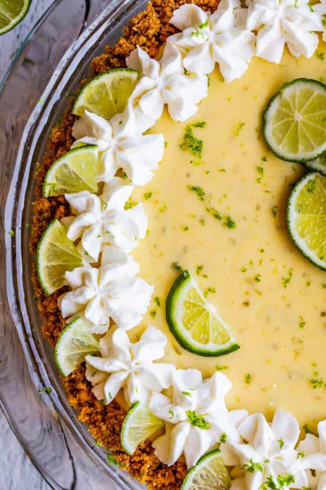 a key lime pie with a graham cracker crust, whipped cream, and lime slices.