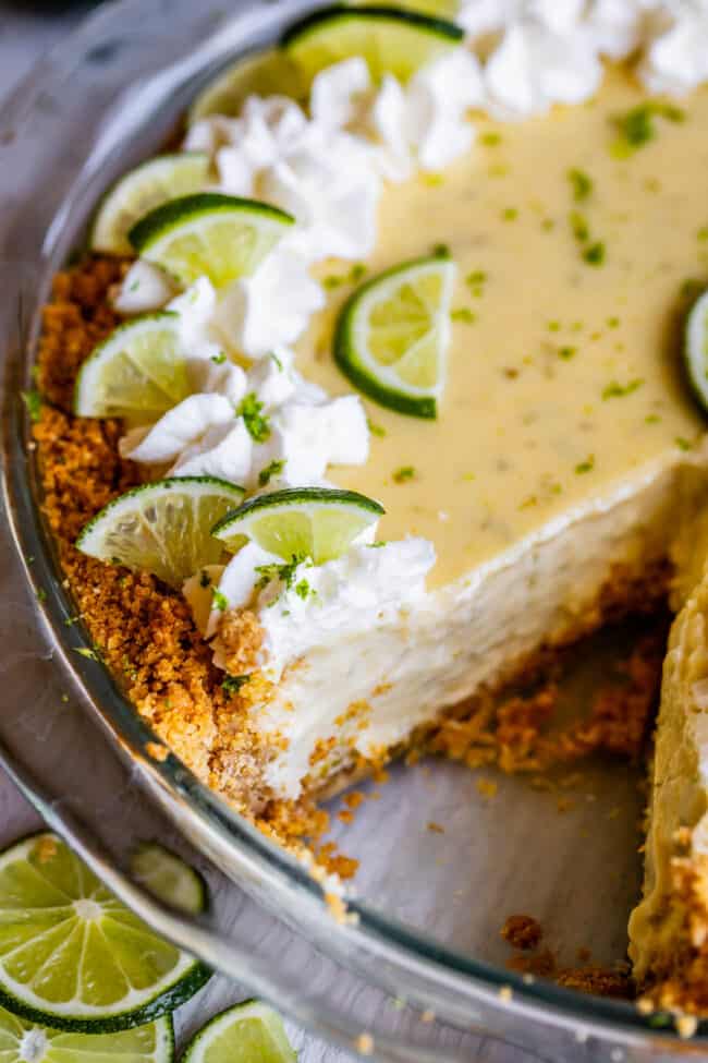 a key lime pie with whipped cream and lime slices with a piece cut out.